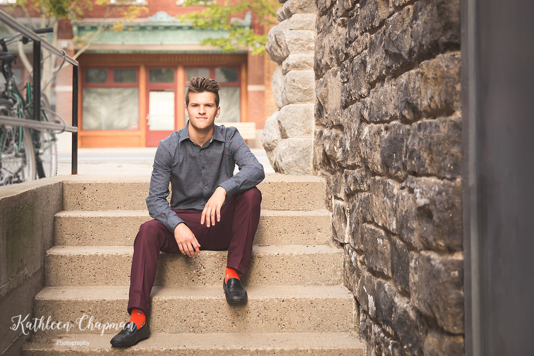 Senior guy smiling sitting on steps in brick alley in Potsdam NY St. Lawrence County family photographer