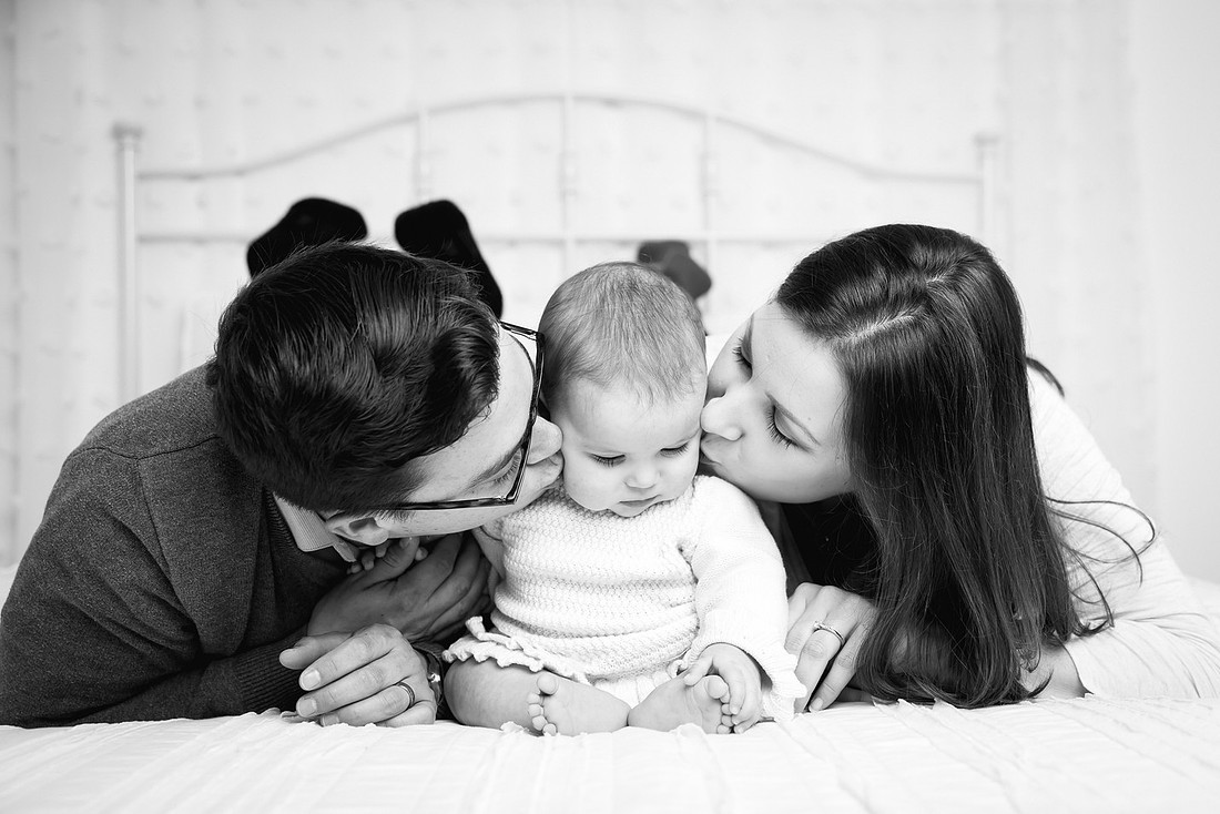 parents kissing baby girl on bed potsdam ny child photographer